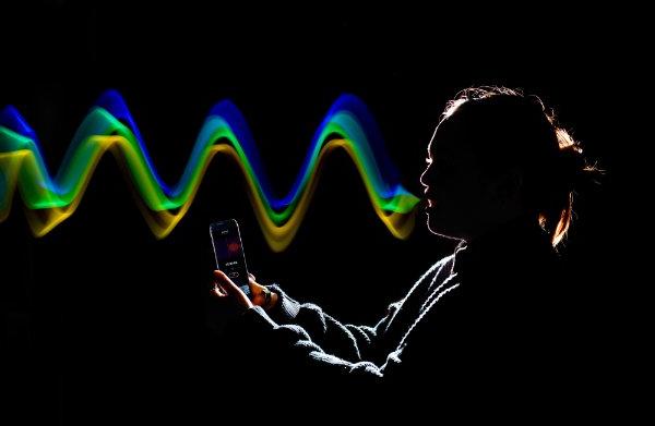 A photo illustration of colorful "sound waves" coming from a person's mouth while holding a cell phone.