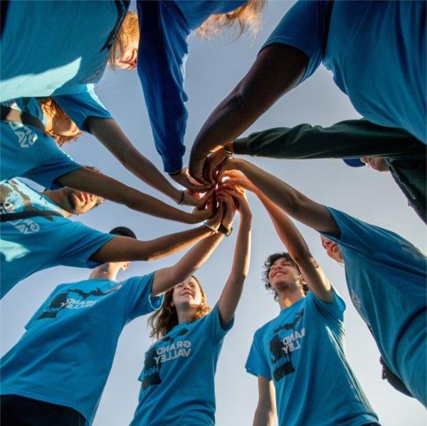 A group of RAs wearing matching blue shirts put their hands together in a circle formation.