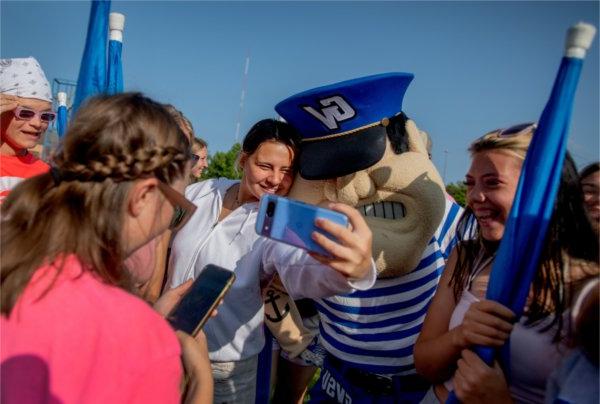  Marching band members surround a college mascot to take selfie photos with their cellphones. 