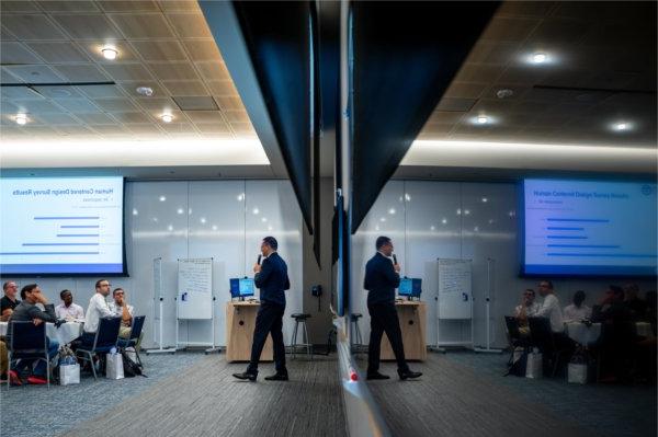  A faculty member wearing a suit is reflected in a white board as he speaks to an audience. 