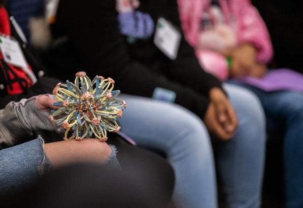 A student holds an expansion ball in their lap that is being used as an item to hold when it's your turn to speak. 